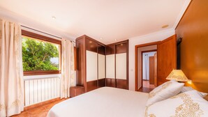 Ein Schlafzimmer mit einem großen Bett, einem Fenster mit Vorhängen, einem Holzschrank und einer Lampe.