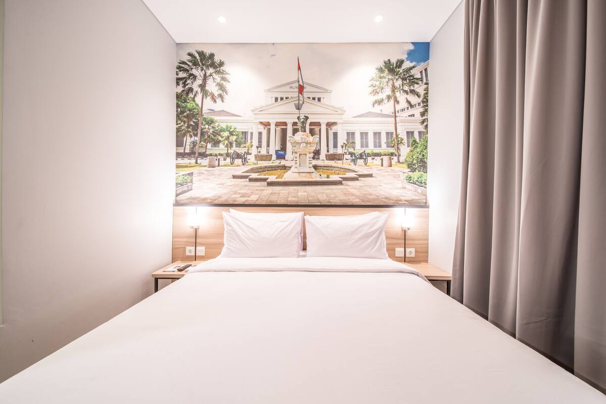 A hotel room with a bed, nightstands, and a mural of a building and palm trees.