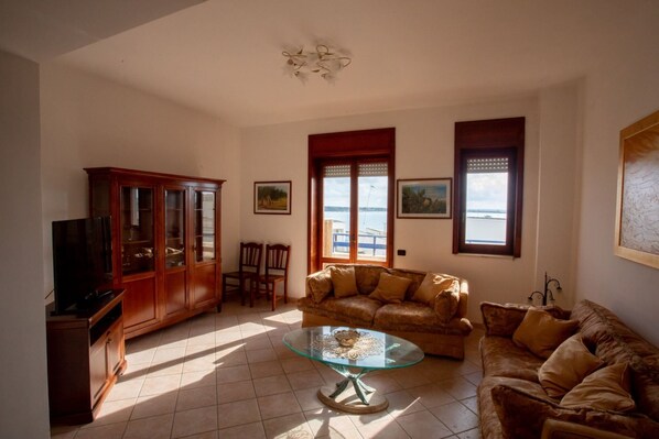 A living room with a glass coffee table, a brown leather sofa, a wooden cabinet, and a television.