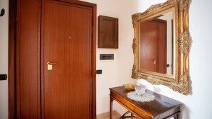 Eine Holztür, ein kleiner Tisch mit einer Zier-Schale und einem Glasobjekt, sowie ein Spiegel mit aufwendiger Rahmung.
