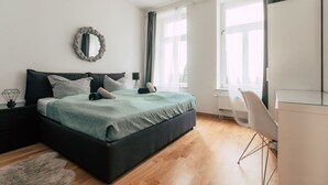 A modern bedroom with a large bed, a bedside table, a mirror, and a window with curtains.