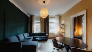 A modern living room with a sectional sofa, a round dining table, and a hanging light fixture. - *Grand Botanical* 4-room apartment with kitchen - Luga Homes - Townhouse (Leipzig)