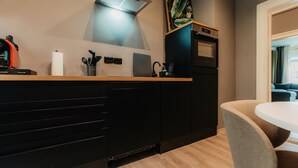 A modern kitchen with black cabinets, a wooden countertop, a built-in oven, and a visible vent hood. - *Grand Botanical* 4-room apartment with kitchen - Luga Homes - Townhouse (Leipzig)