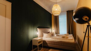 A bedroom with a bed, bedside table, lamp, and a hanging light fixture. - *Grand Botanical* 4-room apartment with kitchen - Luga Homes - Townhouse (Leipzig)