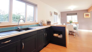 A modern kitchen with a built-in sink, a kettle, and a small dining area with a table and chairs. - 3 Croftside (Aviemore)