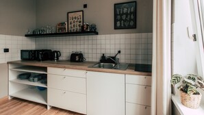 Moderni keittiö, jossa on valkoiset kaapit, puinen työtaso ja laatoitettu välitila. Keittiössä on hyllyjä, joilla säilytetään keittiötarvikkeita, sekä mikroaaltouuni.