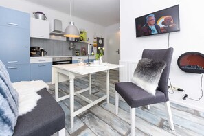 Moderni keittiö, jossa on valkoiset kaapit, ruokapöytä ja seinälle asennettu televisio.