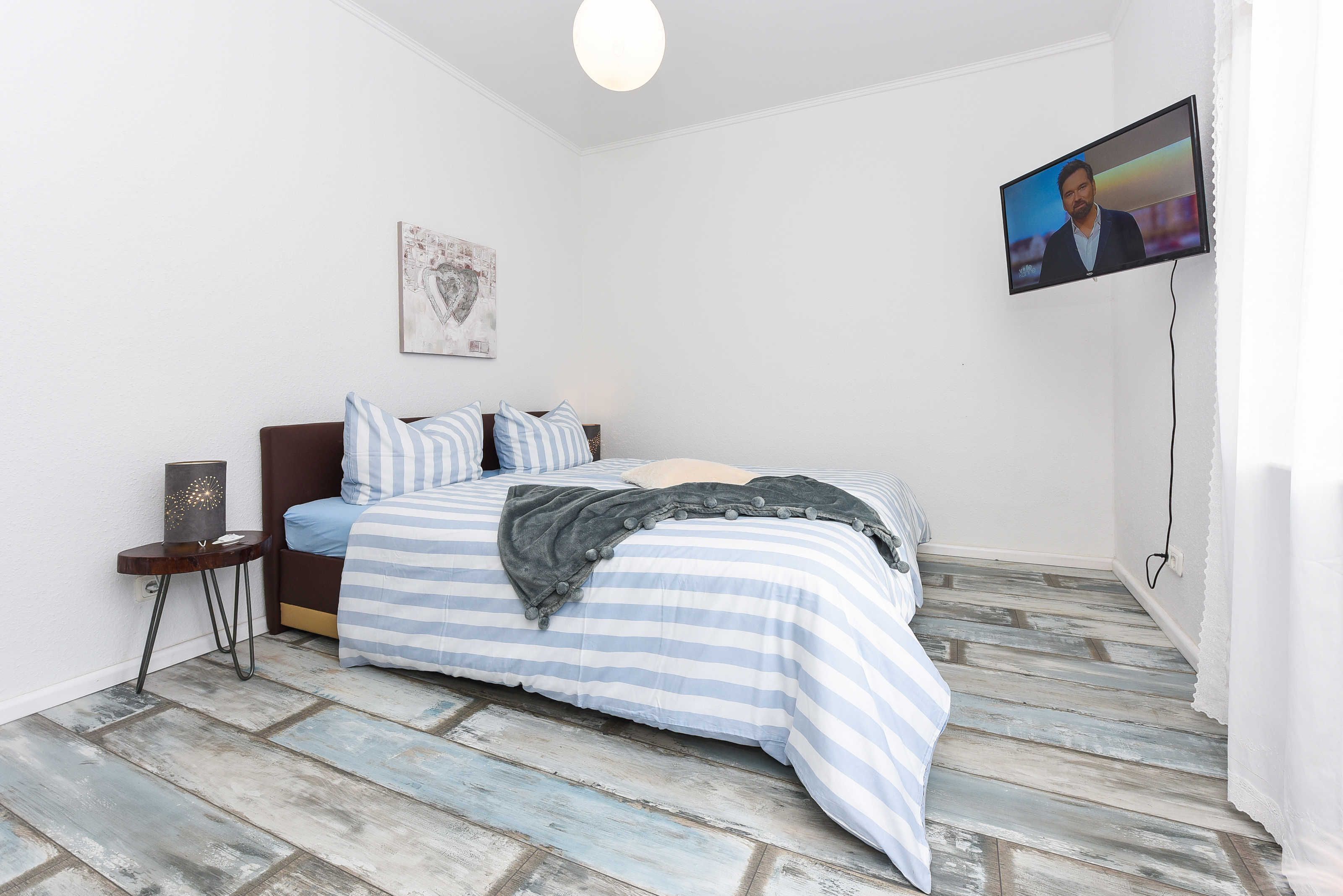 Une chambre à coucher avec un lit, une télévision, une petite table et un tableau accroché au mur.