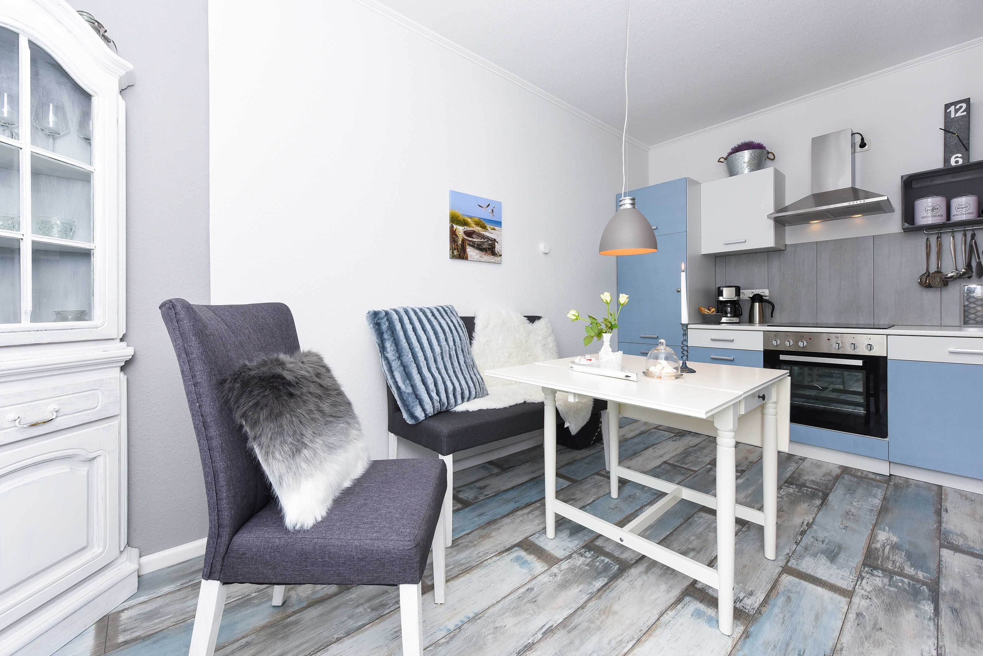 A modern kitchen with white cabinetry, a dining table, and a bench with a fur throw.