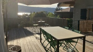 A wooden deck with a table and chairs, a large umbrella, and a view of the mountains. - Maison de Style Savoyard (Menthon-Saint-Bernard)