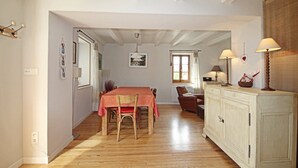 A dining area with a wooden table and chairs, a white cabinet with lamps, and a window with curtains. - Maison de Style Savoyard (Menthon-Saint-Bernard)