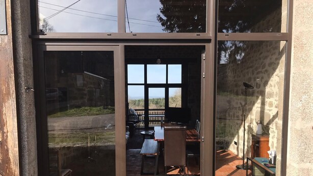 A modern building with large glass doors leading to an outdoor patio area. - Large house in the Morvan (Lormes)