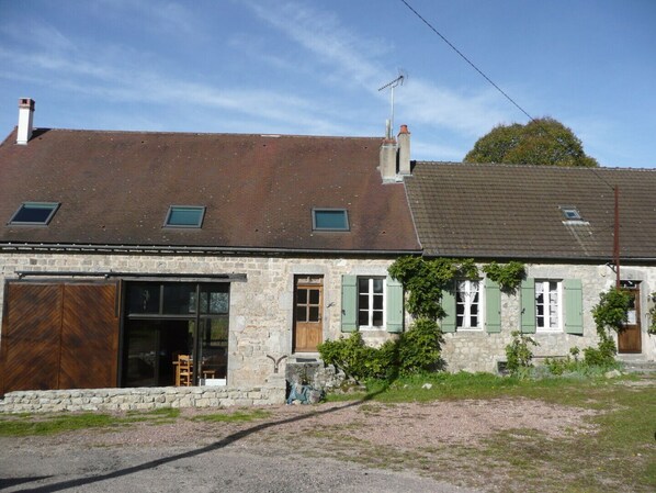A stone building with a large wooden door, a small window, and a chimney. - Large house in the Morvan (Lormes)