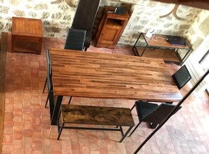 A wooden dining table with chairs, a bench, and a small cabinet in a room with a stone wall and tiled floor. - Large house in the Morvan (Lormes)