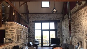 A spacious living area with stone walls, a wooden ceiling, a large window, and a TV. - Large house in the Morvan (Lormes)