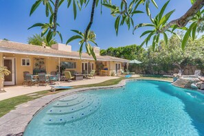 Une piscine à bord incurvé, entourée d’une terrasse avec des chaises et une table.