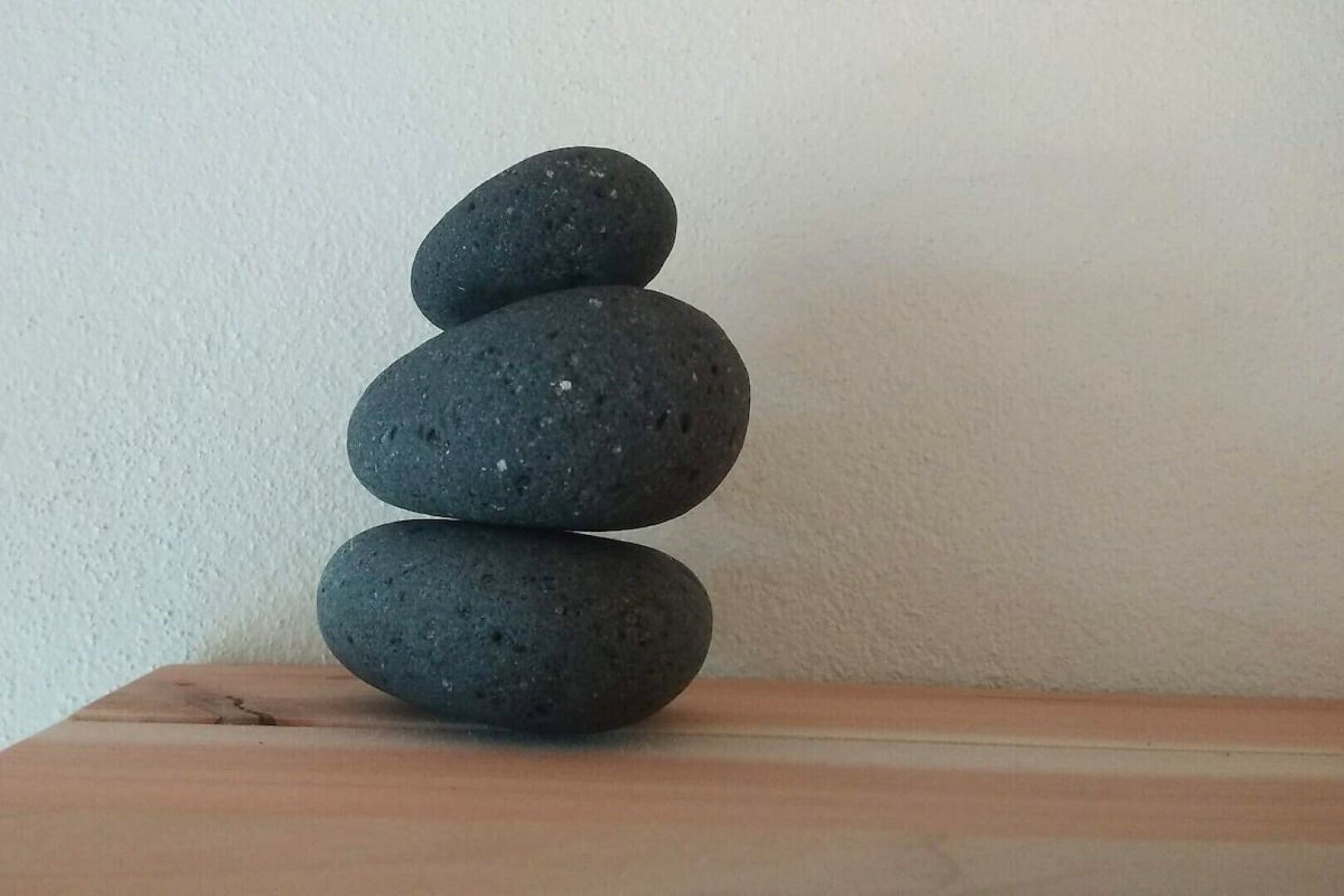 Trois pierres empilées sur une surface en bois, adossées à un mur uni.