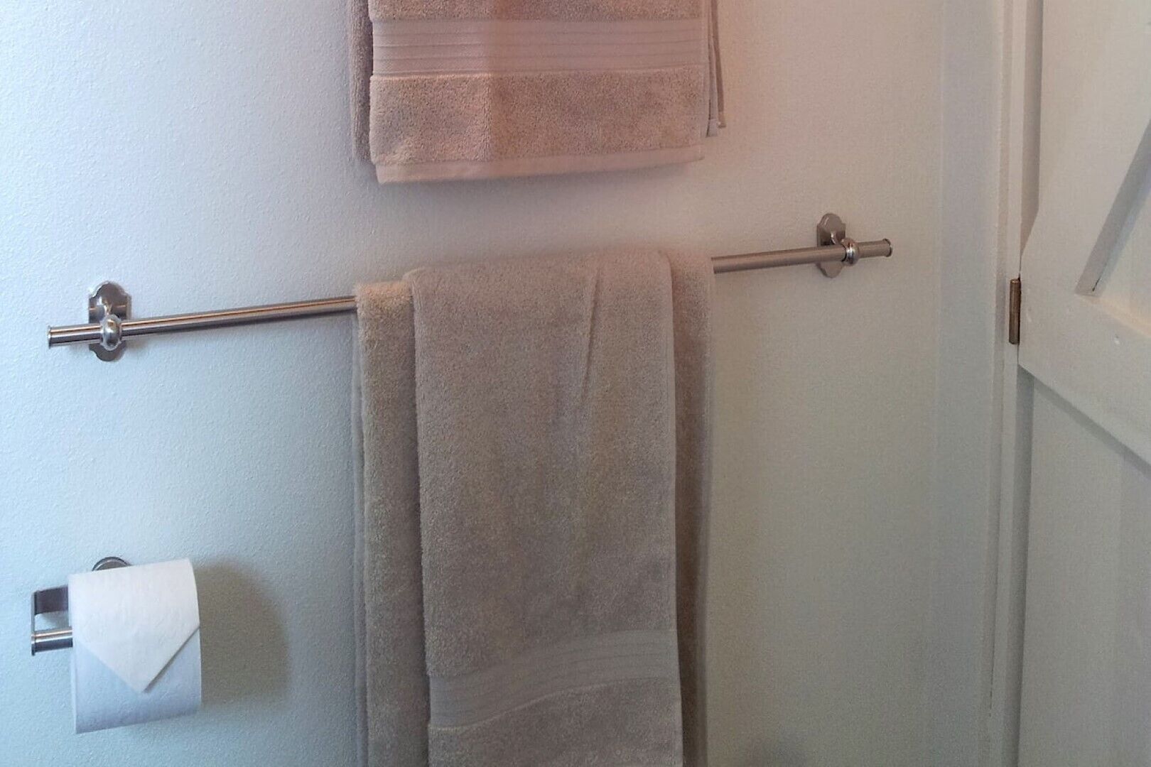 A bathroom with a towel rack holding two towels and a toilet paper holder.