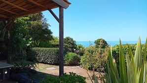 A covered outdoor area with a view of the sea, surrounded by lush greenery and a wooden pergola.