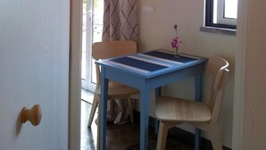 A room with a blue table and a chair, a small vase with a flower, a window, and a door.