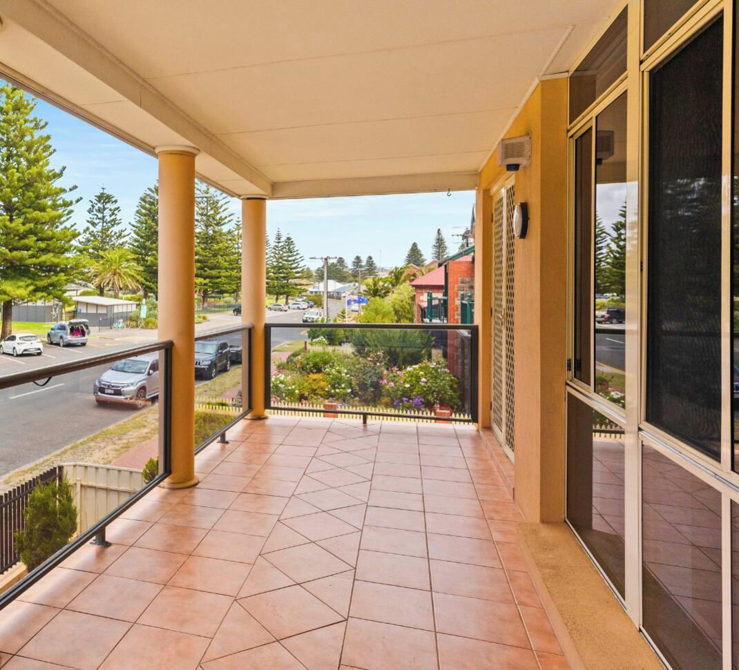 A covered balcony with a view of a street and greenery.