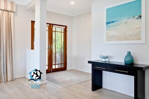 A spacious room with a wooden door, a black console table with decorative items, and a beach-themed painting on the wall.