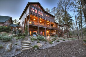 A log cabin with a two-story balcony, stone steps, and a wooden pergola.