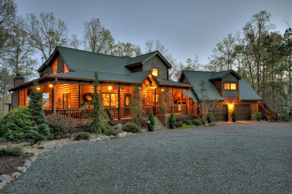 A log cabin with a metal roof, a porch, and a gravel driveway.