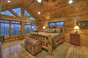 A log cabin bedroom with a large bed, a chest of drawers, and a small cabinet.