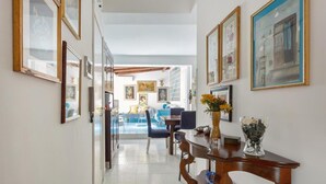 A hallway with framed artwork on the walls, a dining area with a table and chairs, and a view into a room with a pool.