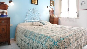 A bedroom with a blue wall, a bed with a white headboard, and a window with white curtains.