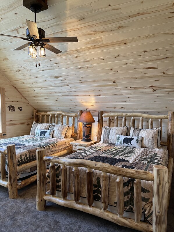 Un dormitorio tipo cabaña de madera con techo de madera, un ventilador de techo y dos camas con ropa de cama a juego.
