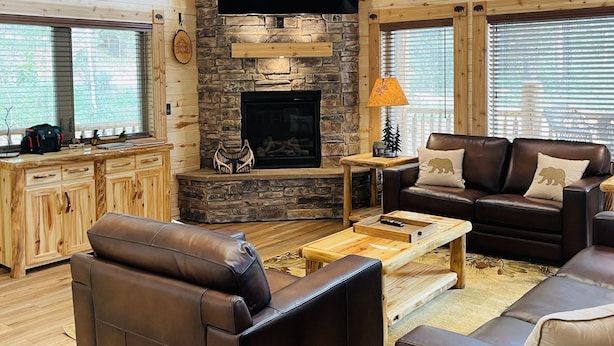 A spacious living room with a stone fireplace, leather sofas, and a large TV mounted on the wall.