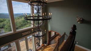 A staircase with a wooden handrail and a chandelier with multiple candle-like lights. - Spectacular Estate with Breathtaking Views (Banner Elk)