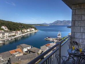 A balcony with a table set for breakfast, overlooking a coastal town with buildings and a body of water. - Apartments Snjezana (Selca)