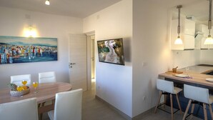 A modern kitchen with a dining area, featuring a wooden table, white chairs, and a painting on the wall. - Apartments Snjezana (Selca)