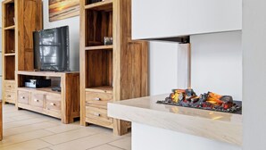 Una cocina moderna con armarios de madera, televisor integrado y encimera de mármol con un elemento decorativo de fuego.