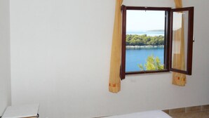 A room with a bed, a window with curtains, and a view of a lake and trees. - A2 - apt Near Beach With Terrace and the sea View (Blato)