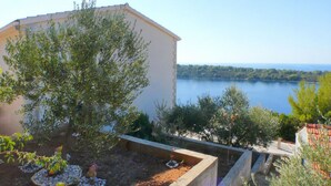 A garden with a tree, a small pond, and a building with a view of the sea.