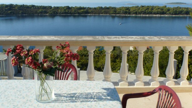 A balcony with a table and chairs, overlooking a calm lake with a distant island.