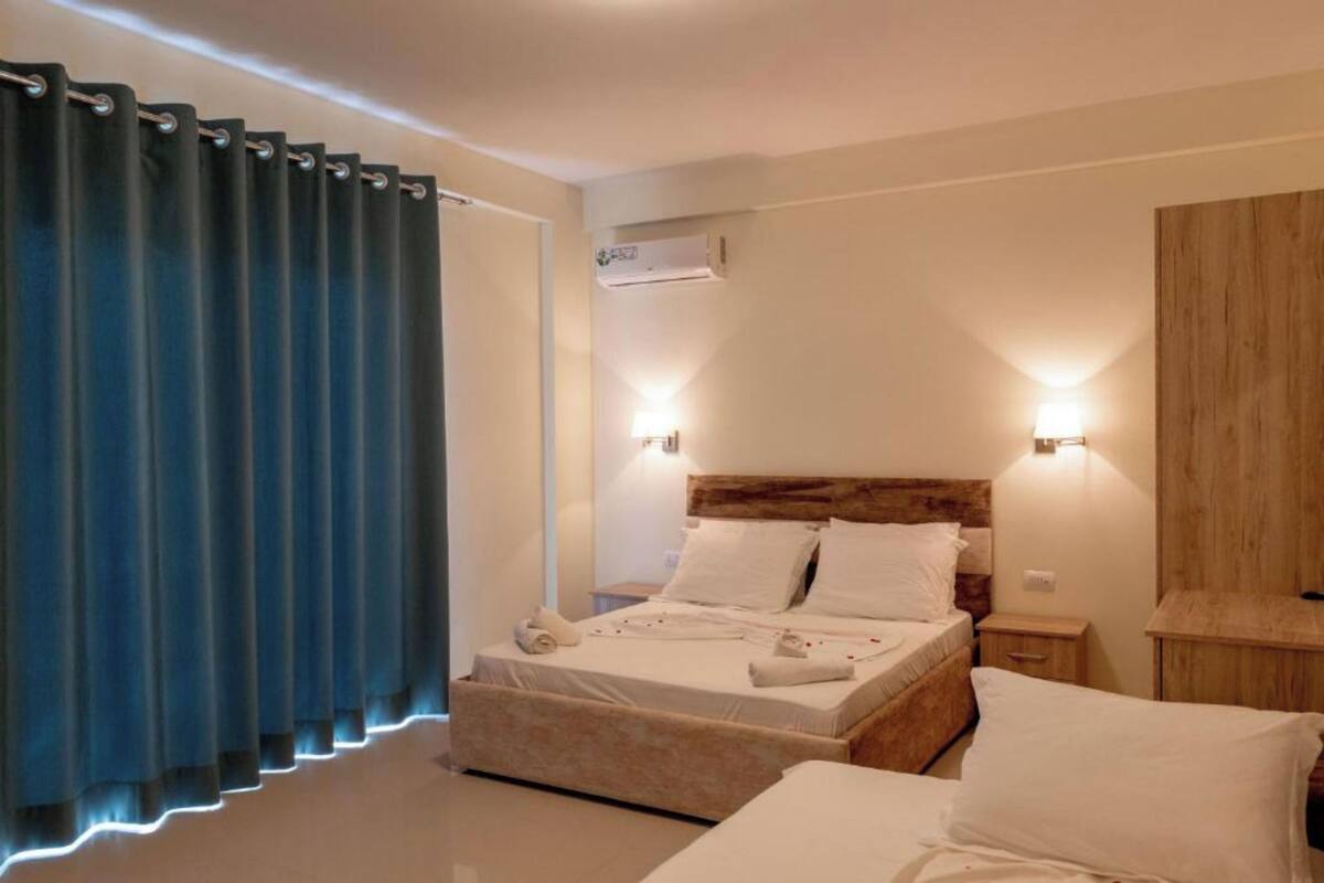 Un dormitorio con cama, mesitas de noche, un equipo de aire acondicionado y una cortina.