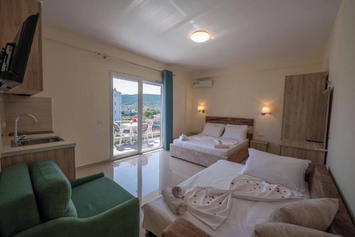 Una habitación de hotel con balcón, kitchenette y cama con cabecera de madera.