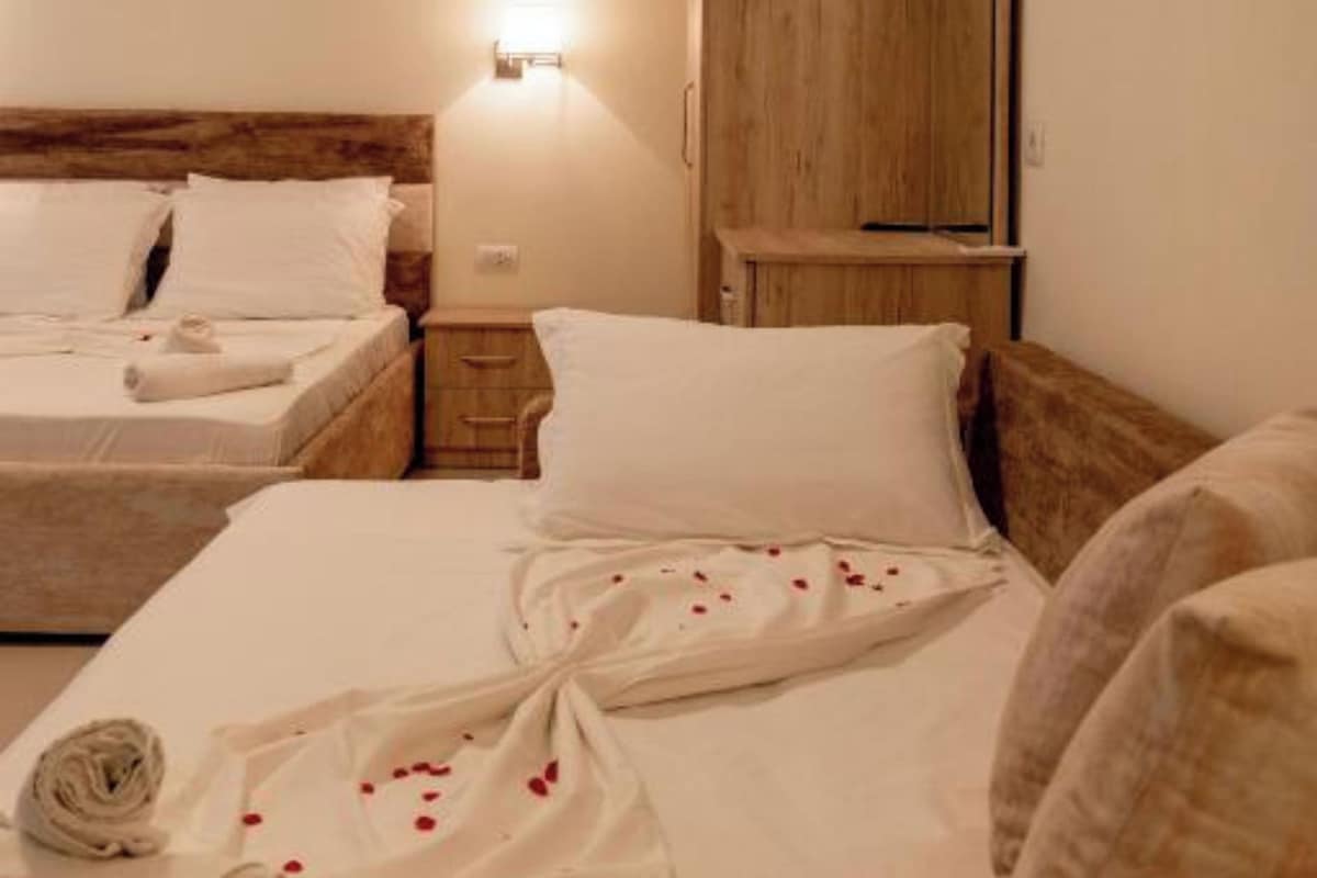 Une chambre d’hôtel avec deux lits, une armoire en bois, une table de chevet et une lampe fixée au mur.