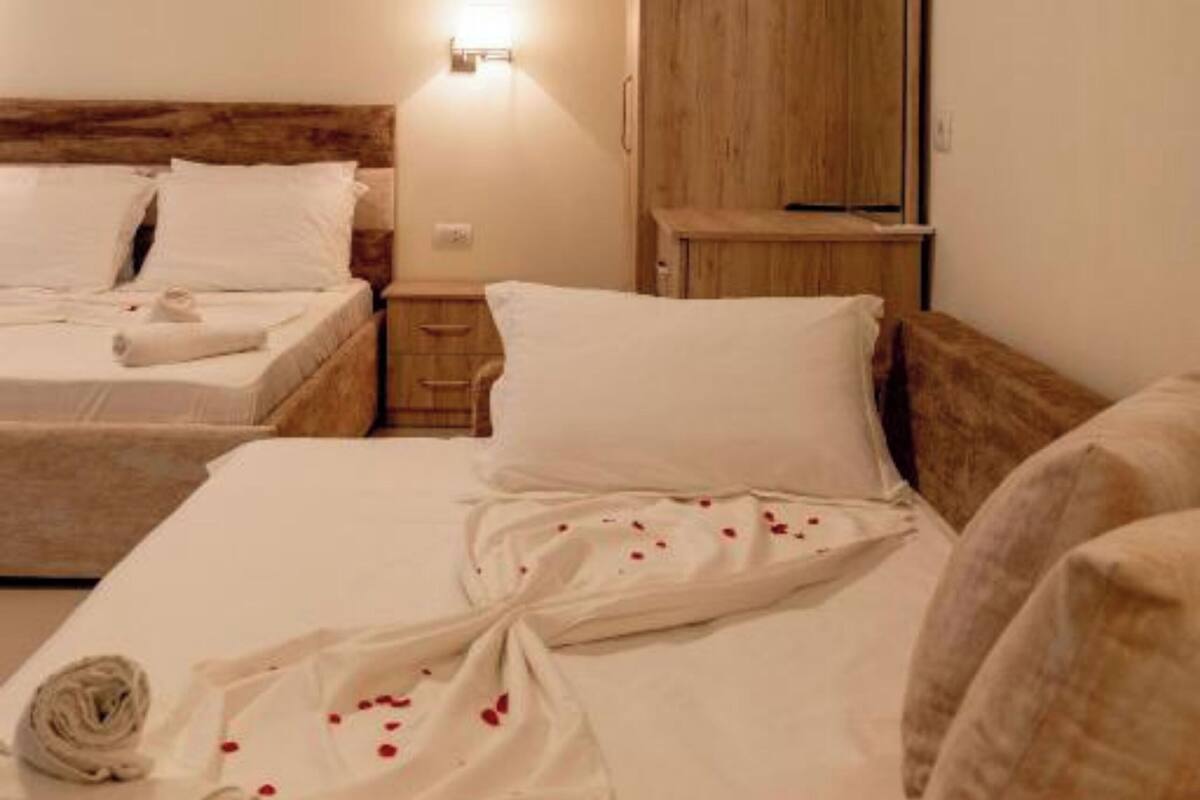 Habitación de hotel con dos camas, un armario de madera, una mesita de noche y una lámpara fijada a la pared.
