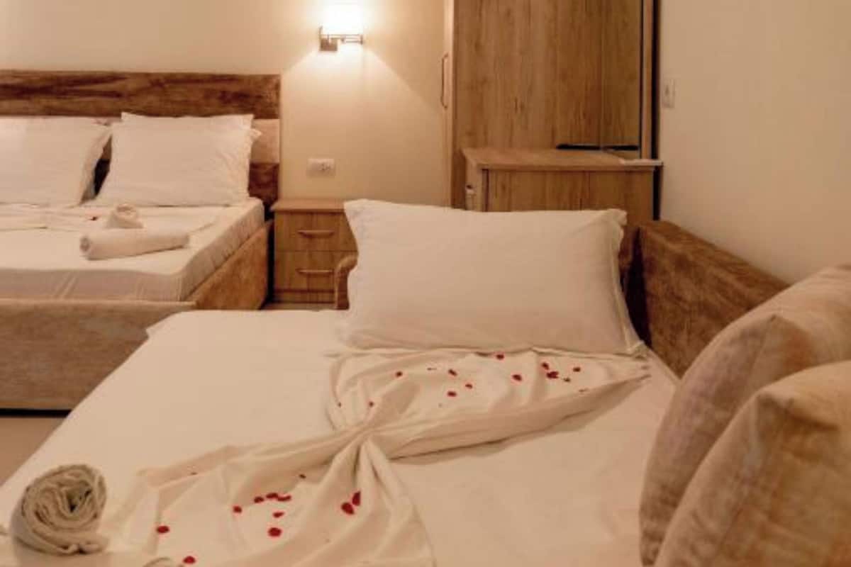 A hotel room with two beds, a wooden wardrobe, a nightstand, and a wall-mounted light.