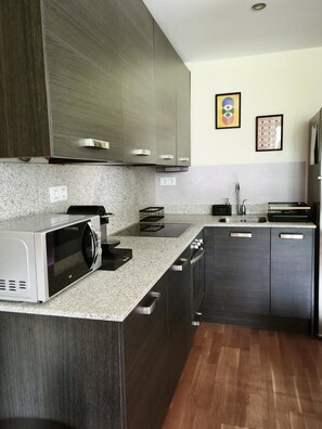 A modern kitchen with dark cabinetry, a granite countertop, a built-in microwave, and a stainless steel sink.