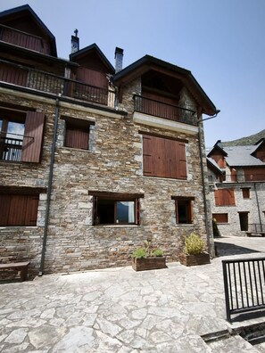 A stone building with wooden shutters, a balcony, and a paved courtyard.