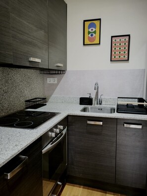 Een moderne keuken met donkere kastjes, een granieten aanrechtblad, roestvrijstalen apparatuur en twee kunstwerken in lijsten aan de muur.
