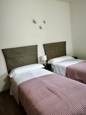 A hotel room with two beds, each with a checkered bedspread, a nightstand with a lamp, and a wall-mounted light fixture.