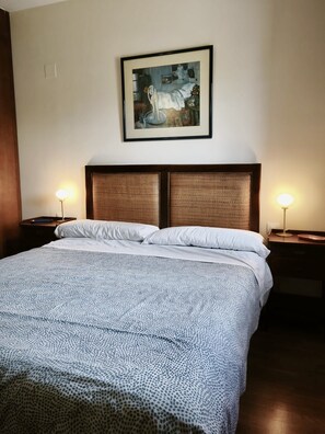 Een hotelkamer met een groot bed, twee bedlampen, een lijst met een schilderij en een houten hoofdeinde.
